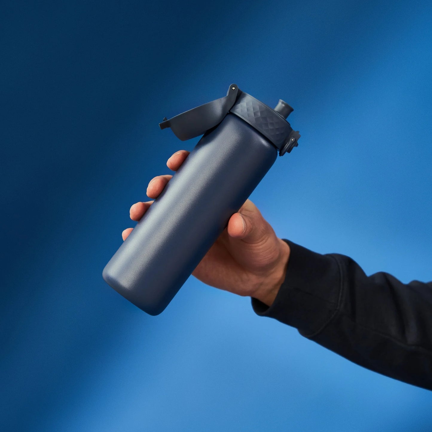 A hand holds a blue water bottle with a flip-top lid against a gradient blue background.