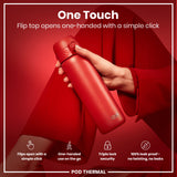 A red thermal water bottle is being held; its flip top opens one-handed via a simple click. The bottle is showcased against a red backdrop. 