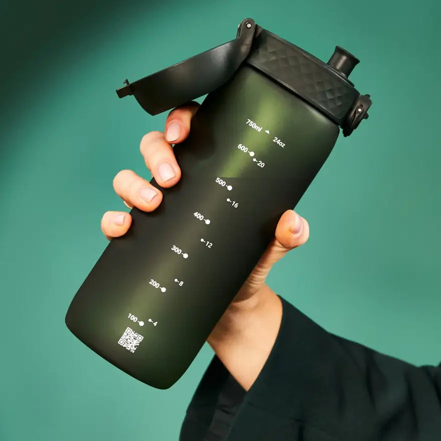A dark-green water bottle, marked with milliliters and ounces, is held by a person against a teal backdrop. 750ml ▲ 24oz; 600 ● 20; 500 ● 16; 400 ● 12; 300 ● 8; 200 ● 8; 100 ● 4. A QR code is also visible at the bottom.