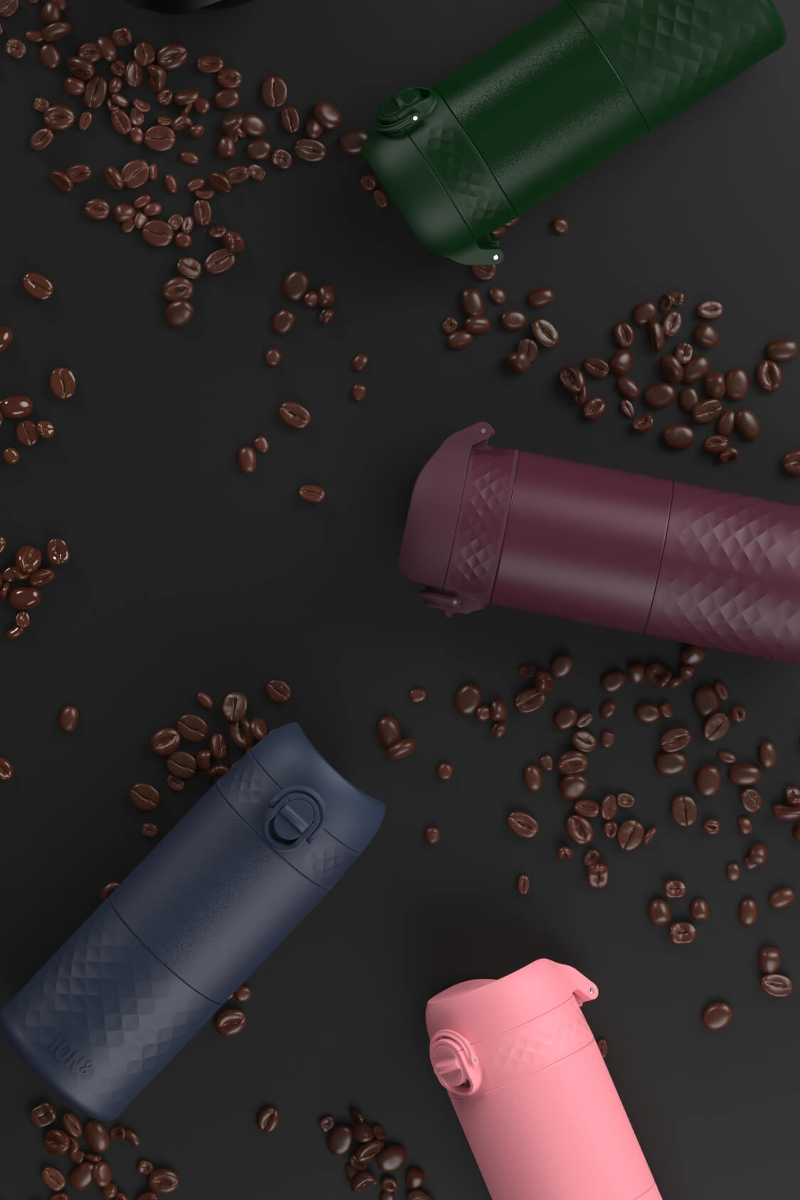 Several portable coffee makers, in various colors, are scattered on a dark surface amongst coffee beans.