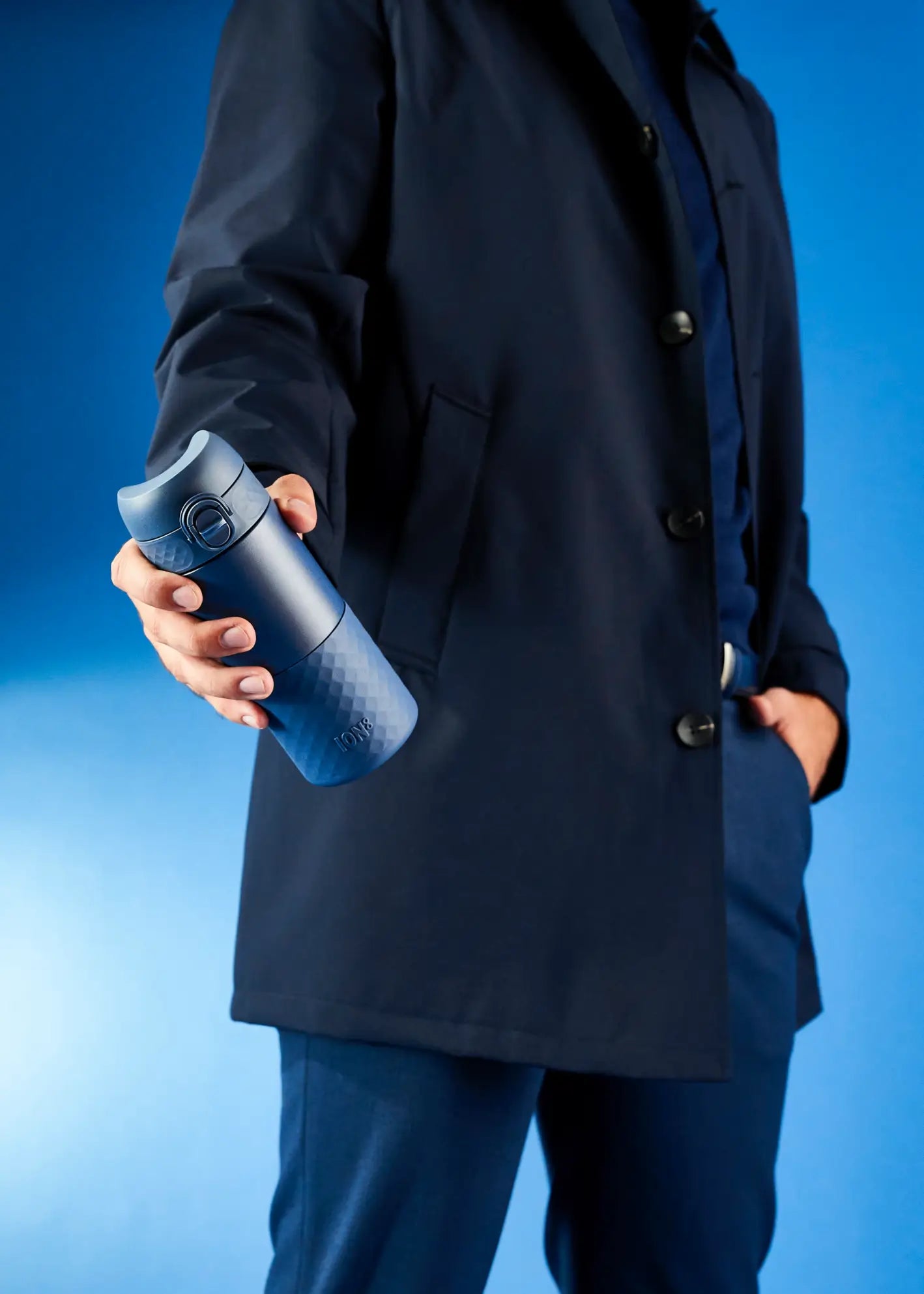 man in long coat holding the ash navy ion8 travel mug