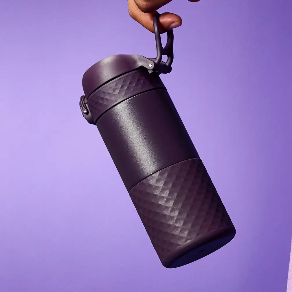 A dark purple thermos is being held against a purple background. The thermos has a textured bottom and a carrying handle.