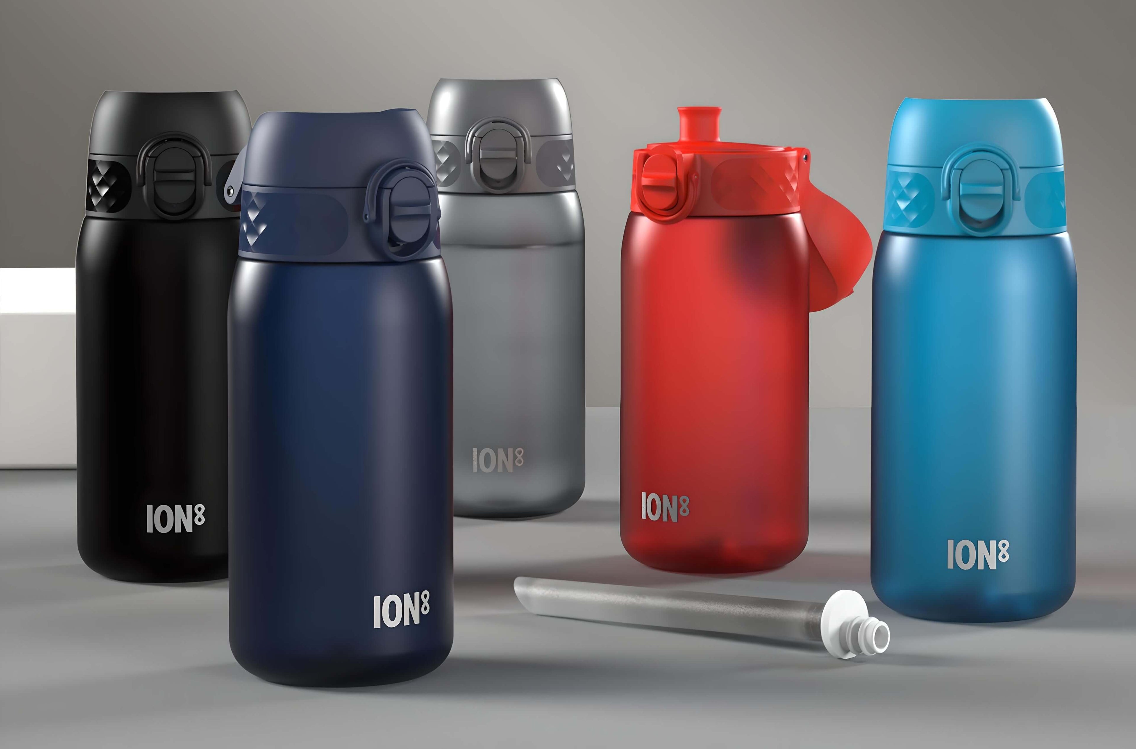 Five ION8 water bottles, in black, navy, silver, red, and blue, sit on a gray surface. Each bottle features a hinged top.
