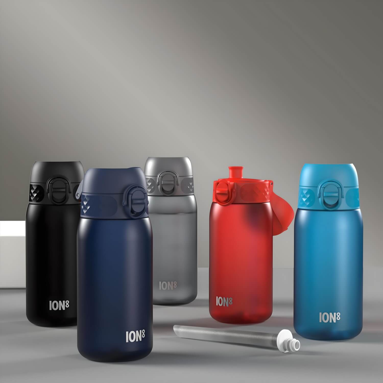 Five ION8 water bottles, in black, navy, silver, red, and blue, sit on a gray surface. Each bottle features a hinged top.