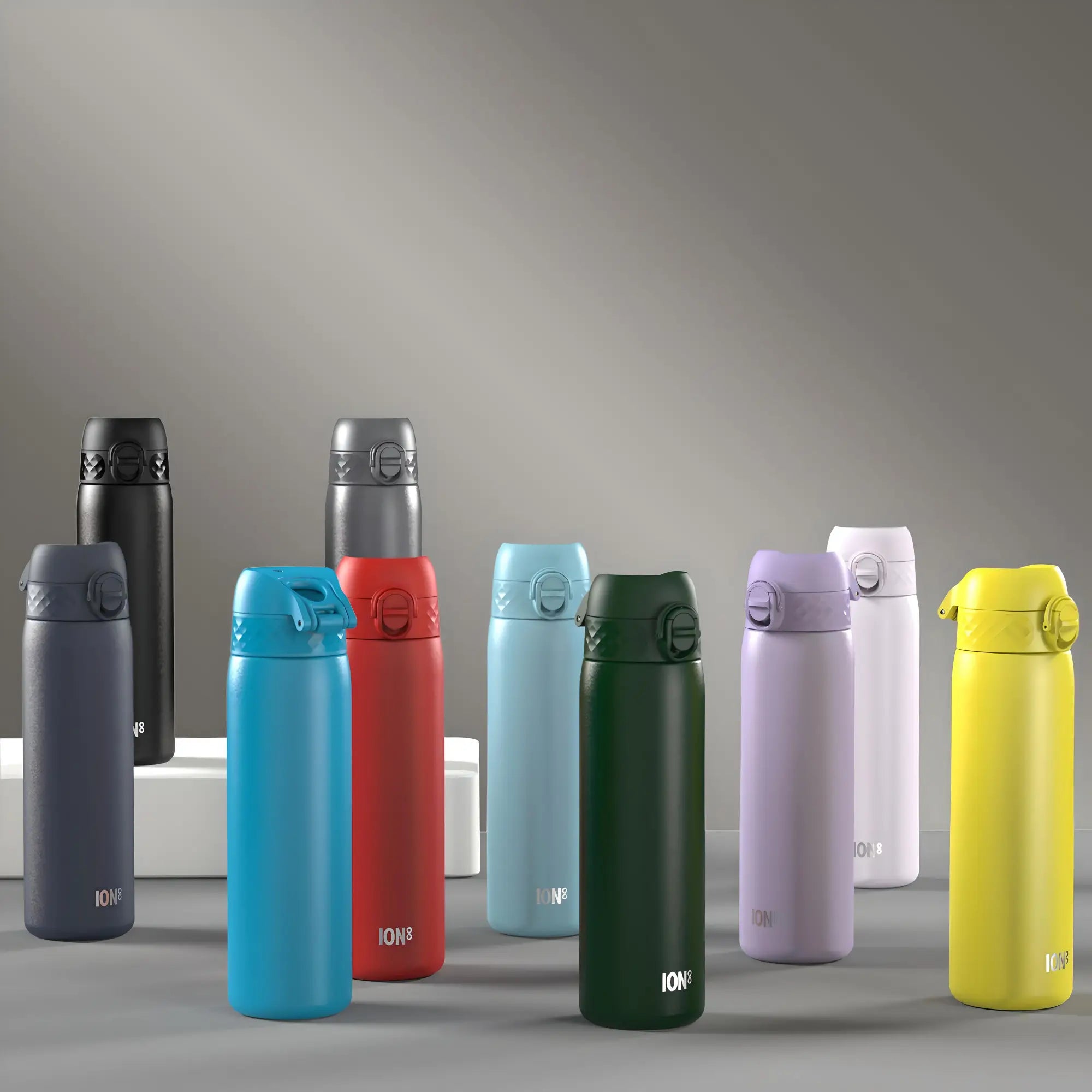 Several ION8 water bottles of various colors are displayed on a gray surface, arranged near small white blocks against a gray background.