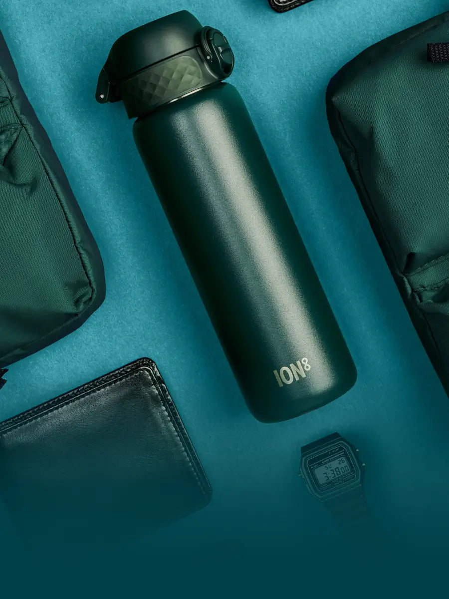 insulated steel bottle in dark green flat laying amongst other dark green and black accessories