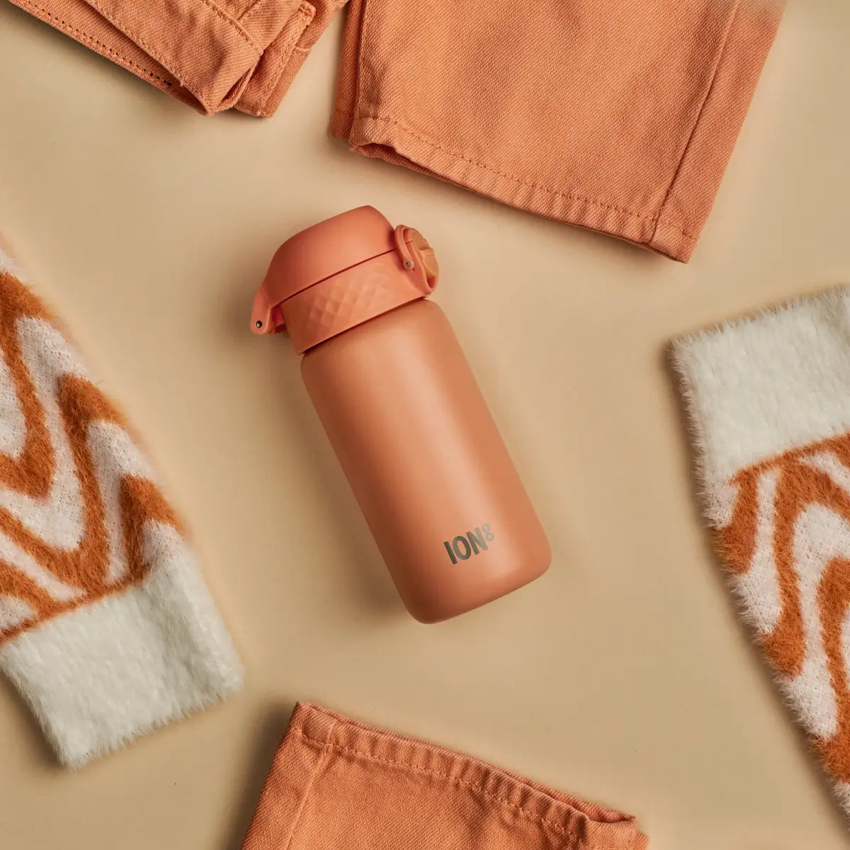coral coloured steel water bottle in a small size flat lay with similar coloured accessories and clothes