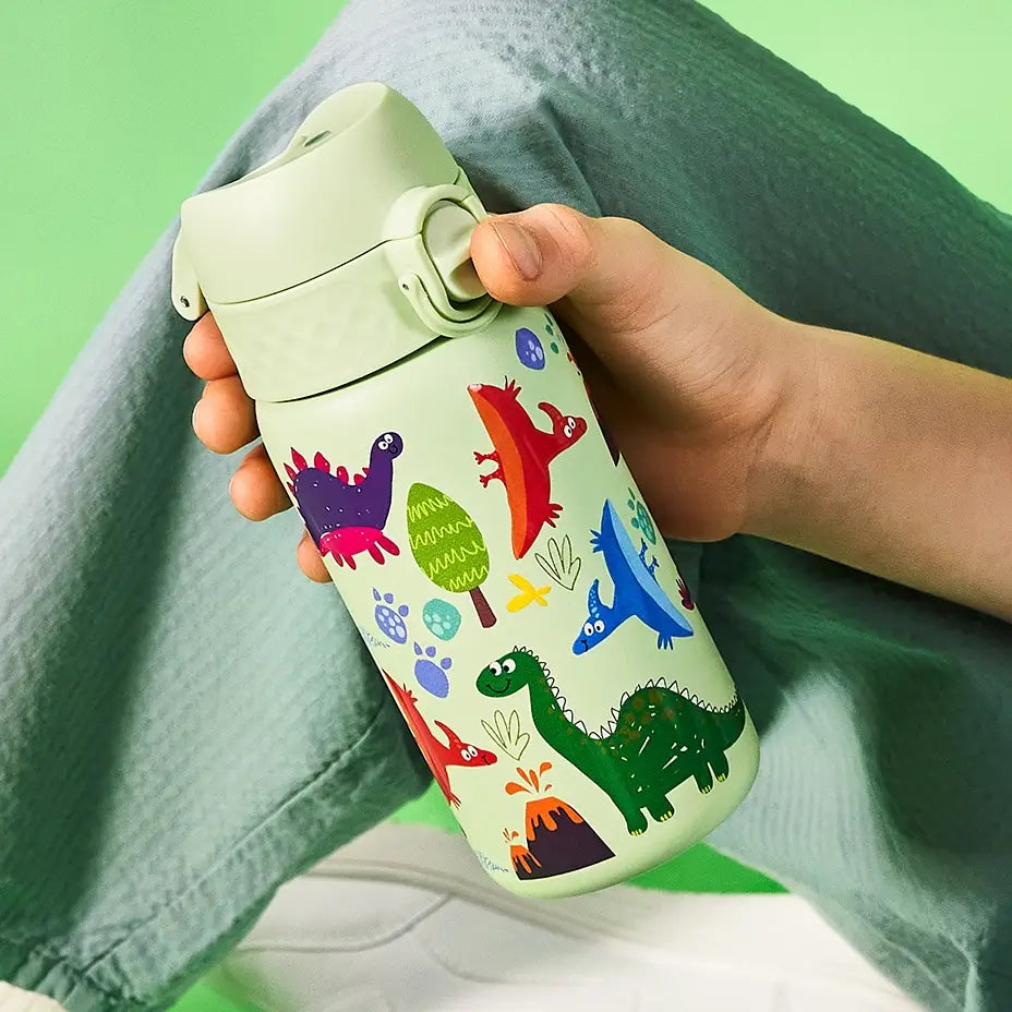 A light-green water bottle, featuring colorful dinosaur illustrations, is held by a child. The bottle has a flip-top lid. The scene is set against a light-green background.