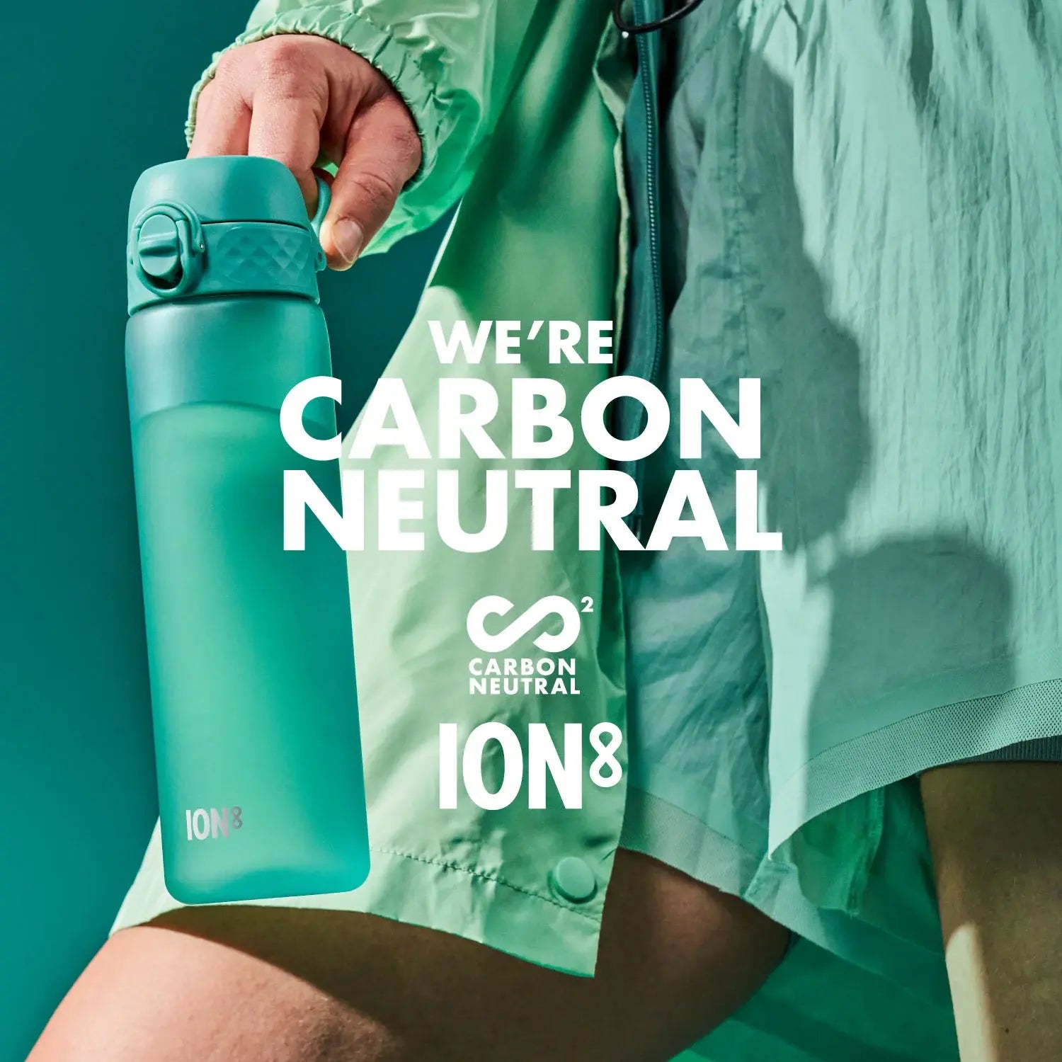 A teal water bottle is held by a person, against a teal background. The text reads: WE'RE CARBON NEUTRAL ∞² CARBON NEUTRAL ION8.